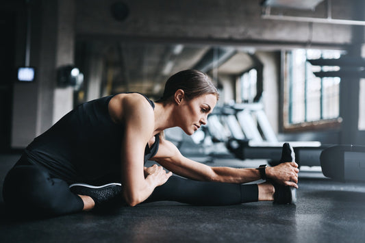 Frau dehnt sich in einem Fitnessstudio, während sie auf den Boden sitzt und ein Bein streckt.